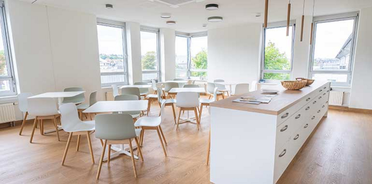 Nexia GmbH | Dresden Blick in einen Pausenraum mit Küchenzeile und mehreren Tischen mit Stühlen.