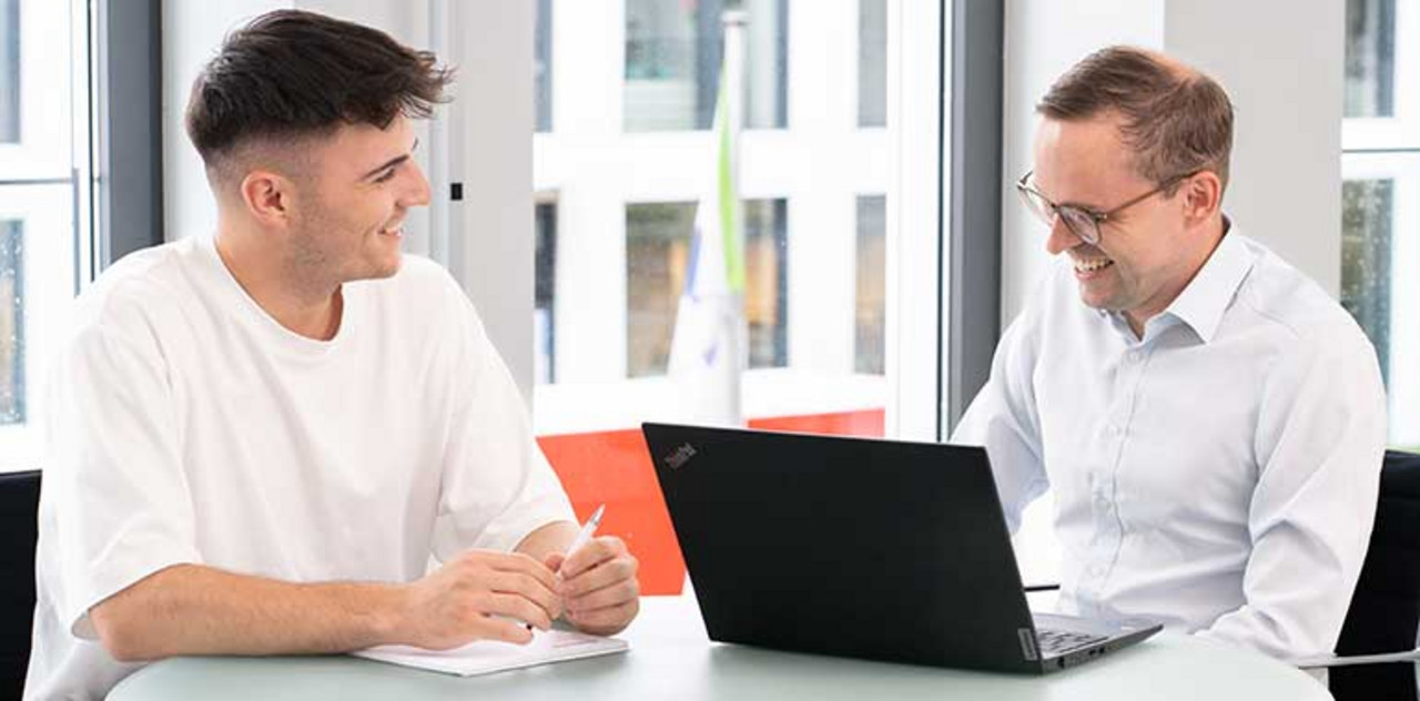 Berufseinsteiger Zwei Personen sitzen mit einem Laptop an einem Tisch.