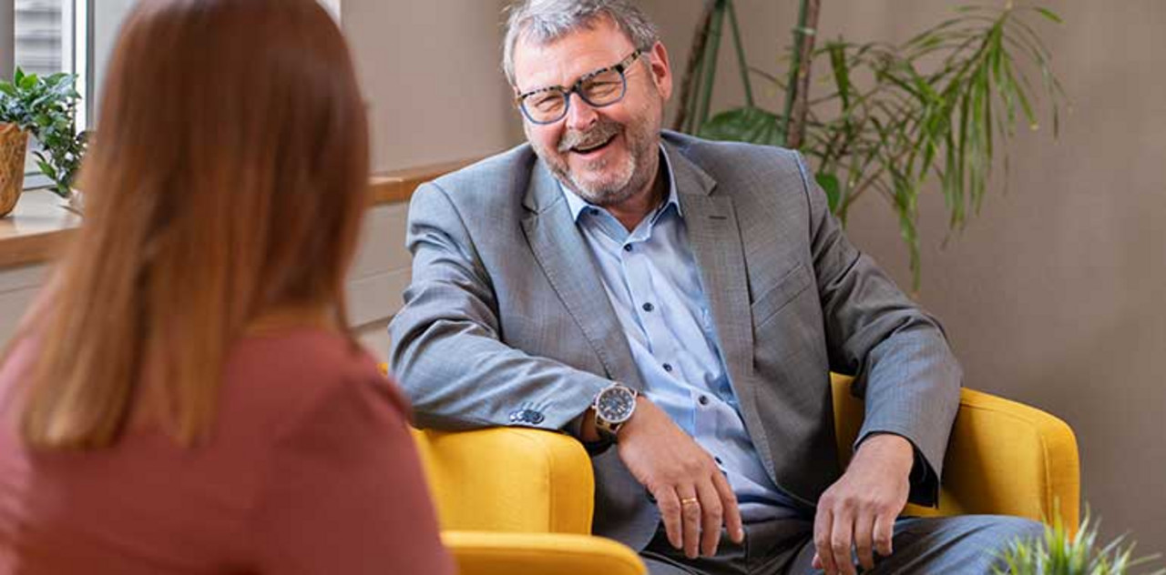 Wir leben Gemeinschaft und teilen Wissen Ein Partner sitzt locker mit einem Mitarbeiter zusammen und lacht.