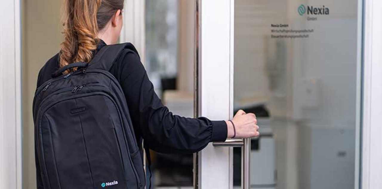 Nexia GmbH | Halle/Leipzig Eine Person mit einem Nexia Rucksack betritt das Büro durch eine Tür.
