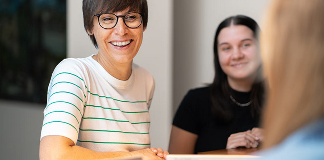 Secondment Drei Personen stehen an Theke zusammen.