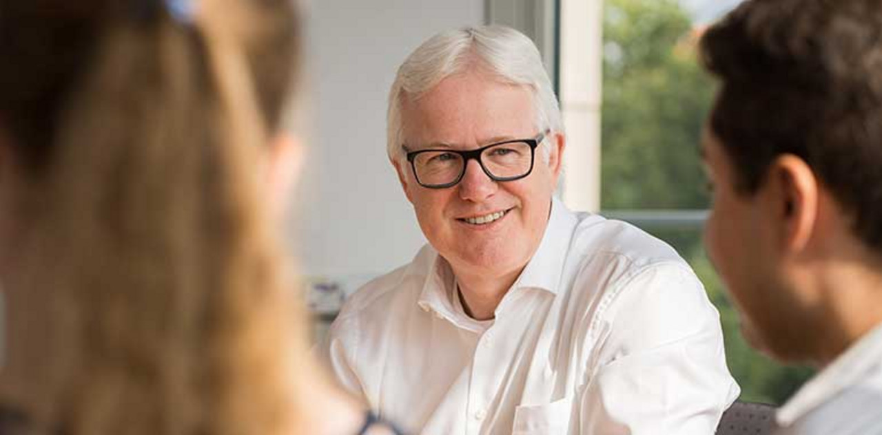 Berufserfahrene Ältere Person sitzt zwischen jüngeren Kollegen.