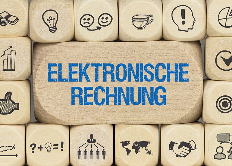 Ein großer Baustein mit der Aufschrift „Elektronische Rechnung“. Darum herum liegen kleinere Bauklötze mit Symbolen wie z.B. Handschlag, Geldscheine und Münzen, einem Pfeil in der Mitte einer Zielscheibe und Glühbirnen.