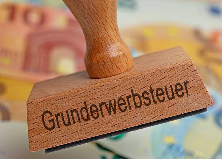 Stempel mit Auschrift "Grunderwerbsteuer" vor Euro-Scheinen.