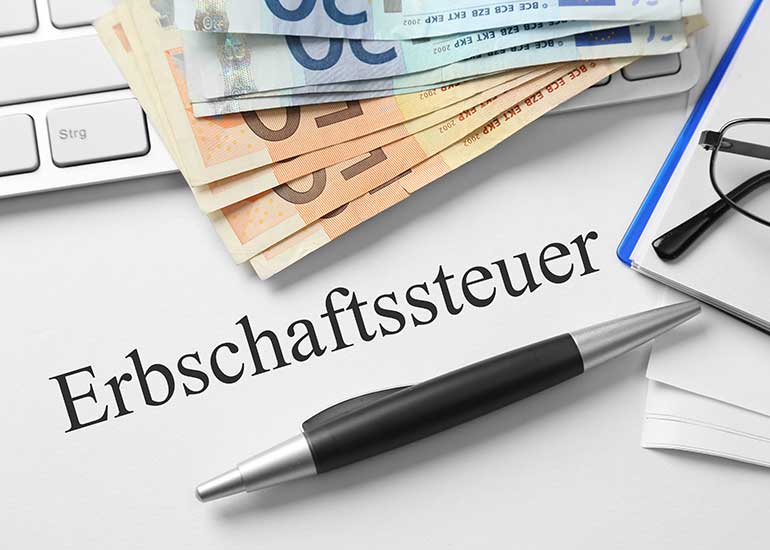 Auf einem Blatt Papier steht "Erbschaftssteuer", daneben liegen eine Tastatur, Euro-Banknoten und ein Kugelschreiber.