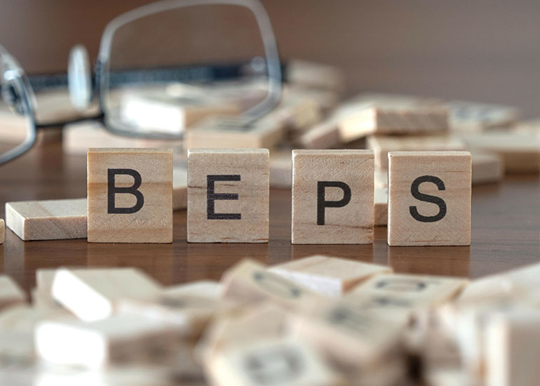 Der Begriff "BEPS" steht für Base Erosion and Profit Shifting. Die Buchstaben "BEPS" stehen jeweils auf einem Holzwürfel auf einem Tisch. Daneben liegen weitere Holzwürfel. Im Hintergrund liegt eine Brille.