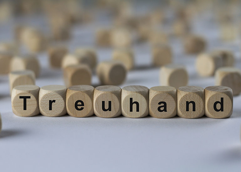 Der Begriff "Treuhand" ist auf Würfeln geschrieben. Jeder Buchstabe ist auf einem Würfel abgebildet. Im Hintergrund liegen weitere Würfel ohne Beschriftung.