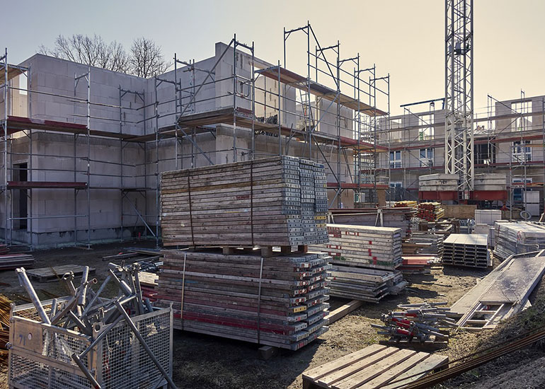 Blick auf die Baustelle eines Mehrfamilienhauses. Zu sehen sind halbfertige Wände und Gerüste.