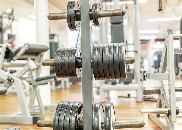 Blick in ein Fitnessstudio. An einer Säule sind Gewichte aufgereiht.