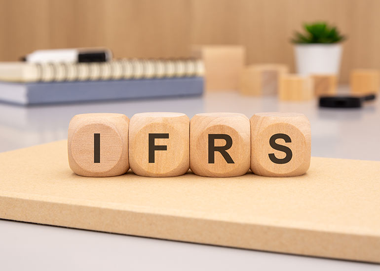 Auf einem Tisch liegen Würfel, auf denen „IFRS“ für „International Financial Reporting Standards“ steht. Jeder Buchstabe steht auf einem Würfel.